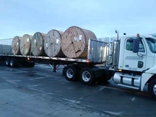 flatbed truck hauling large spools of cable to a NYC job site by Iron Horse Transport